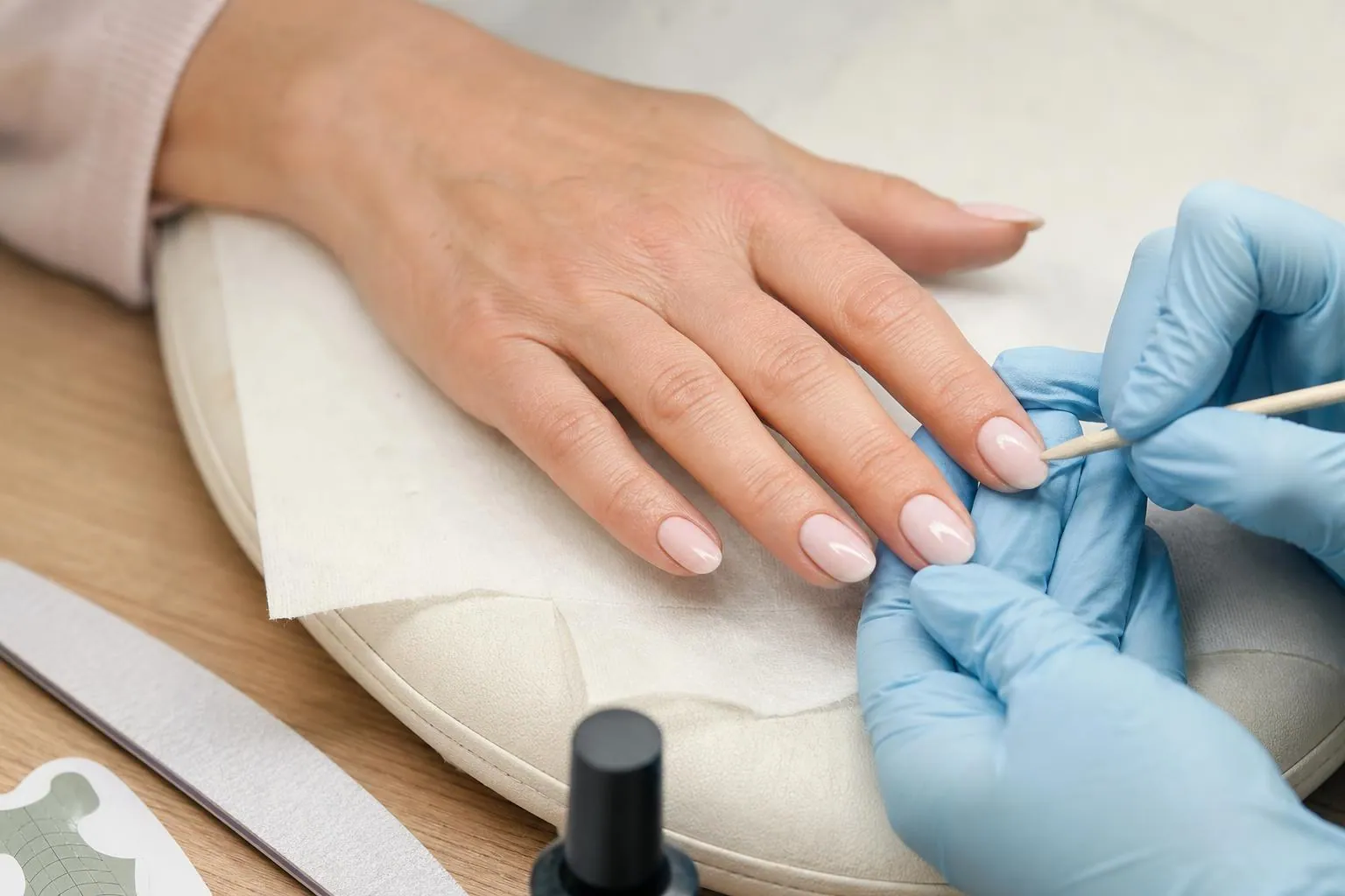 Gros plan sur la main d’une cliente posée sur un coussin clair, un ongle en gel présentant un décollement visible près de la repousse
